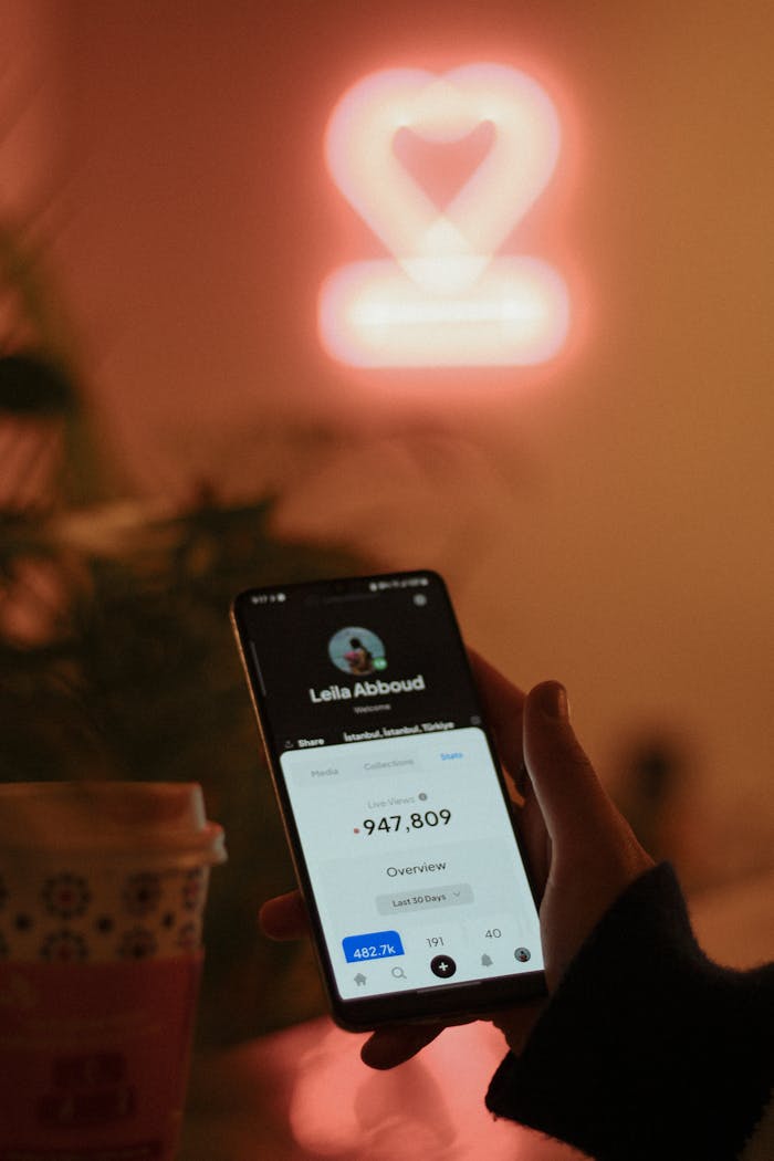 gallery-1 Smartphone display with neon heart backdrop, showcasing modern technology in a cozy setting.