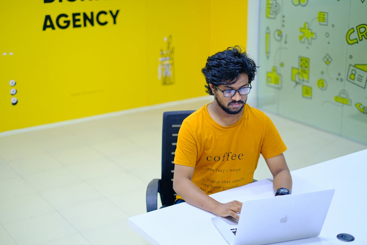 services-02 Young man wearing eyeglasses working on laptop in vibrant digital agency office.